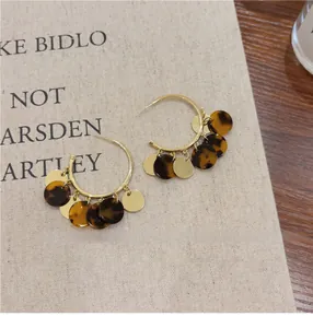 Macro shot of stylish gold hoop earrings featuring elegant dark tortoiseshell and metal discs
