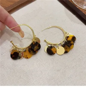 Detail view of gold hoop earrings with dark tortoiseshell and metallic round charms