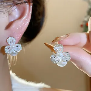 Close-up of elegant zircon flower and pearl earrings shown on model ear and hand