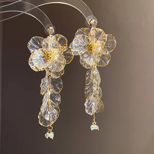 Dettaglio di orecchini a fiore in acrilico trasparente con bordi dorati e nappe.