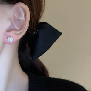 Close-up of an elegant pearl stud earring on model's ear with black bow