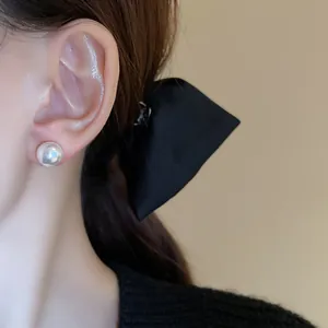 Close-up of elegant pearl stud earring on ear with minimalist black bow detail