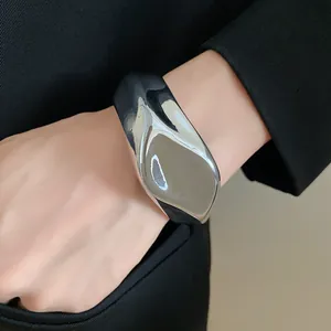 Detalle de brazalete rígido plateado brillante irregular en muñeca con blazer negro
