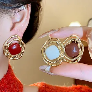Irregular golden metal ear clips with colorful resin centers in red, white and brown.
