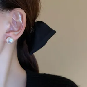 Detail view of an elegant large white pearl stud earring worn on a model's ear lobe
