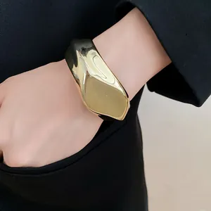 Detalle de un brazalete de metal dorado irregular ancho usado en la muñeca mujer