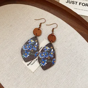 Close-up macro view of teardrop wood earrings with blue floral print on linen fabric