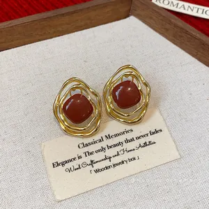 Vintage gold irregular wire-wrapped earrings with red enamel center in wooden box.