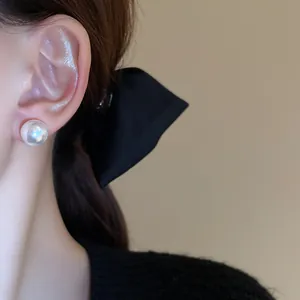 Detailed macro view of a minimalist large white pearl stud earring worn on model's ear
