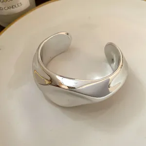 Vista detallada de brazalete plateado irregular con un acabado metálico reflectante