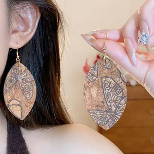 Close-up detail of teardrop leaf earrings featuring vintage butterfly print on cork texture