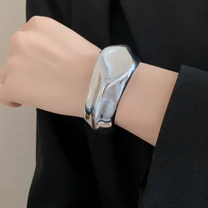 Vista detallada de un brazalete plateado irregular con diseño de pliegues moderno.