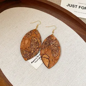 Close-up detail of teardrop earrings with butterfly print on wood texture.