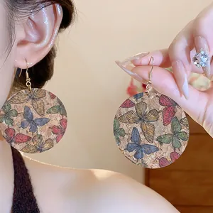 Close-up of bohemian round drop earrings with colorful butterfly prints on cork texture.