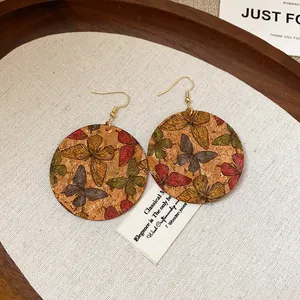 Close-up of cork drop earrings featuring colorful butterfly prints and gold hooks