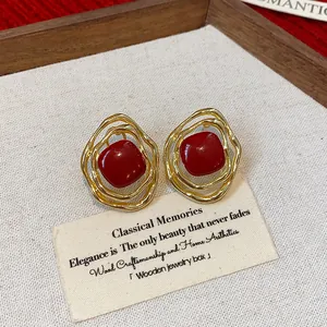 Detailed view of irregular gold-tone clip-on earrings with vibrant red enamel center