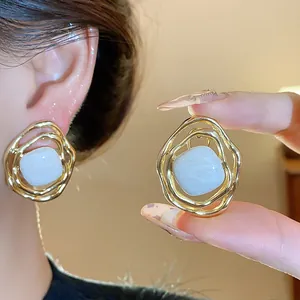 Close-up of gold irregular clip-on earrings with light blue enamel center on model.