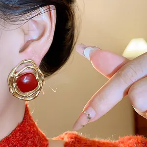 Close-up of irregular gold textured clip-on earring with red enamel stone
