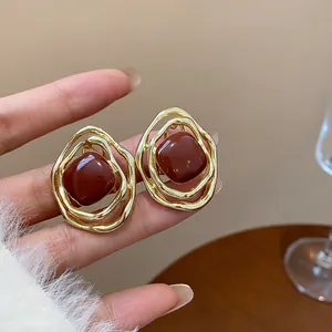 Detail view of irregular gold-tone geometric clip-on earrings with red enamel center