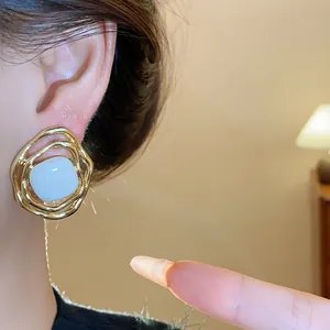 Close-up detail of irregular gold wavy earrings featuring a white enamel center