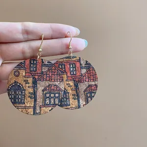 Macro view of cork dangle earrings with architectural house patterns and gold hooks.