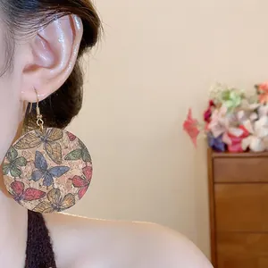 Close-up of large round cork earrings featuring colorful butterfly print on a model.