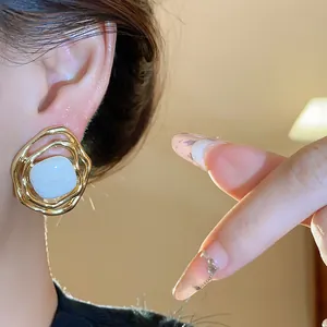 Close-up view of irregular gold-toned ear clips with a square white resin stone insert