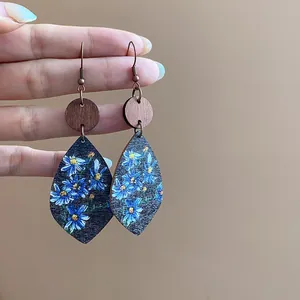 Close-up of elegant teardrop leaf earrings featuring vintage blue floral print on wood texture