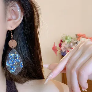 Close-up of leaf-shaped dangle earring with blue floral print on wood texture