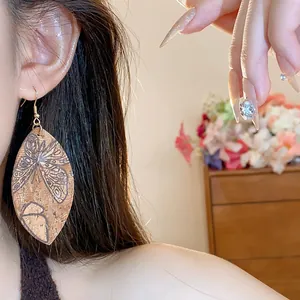 Detailed close-up view of leaf-shaped cork earrings with butterfly print on model