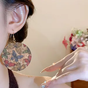 Detailed macro close-up of large cork round dangle earrings with colorful butterfly prints