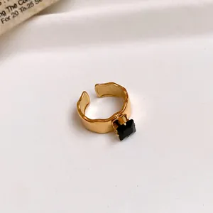Macro detail of a gold stainless steel open ring featuring a square black zircon stone