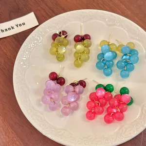 Detalle de cuatro pares de pendientes de cuentas con forma de uva sobre un plato blanco