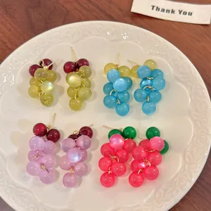 Primer plano de pendientes de resina con forma de racimo de uvas de colores en un plato blanco