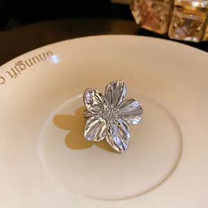 Primer plano detallado de un anillo abierto con forma de flor plateada en un plato