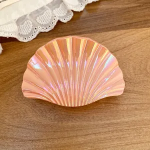 Iridescent shell-shaped hair claw clip with pleated texture on wooden background