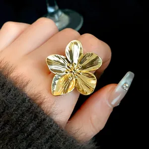 Primer plano detallado de un anillo de flor abierto bañado en oro en el dedo.