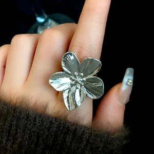 Primer plano de un gran anillo de flor plateado usado en el dedo de una mano femenina.
