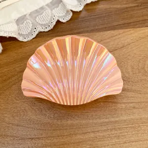 Detailed close-up of pink iridescent seashell-shaped hair claw clip on wooden background
