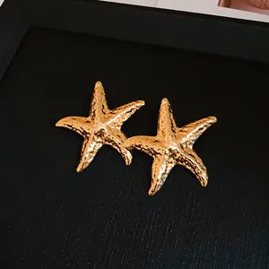 Macro view of gold starfish stud earrings featuring a detailed hammered metal texture