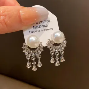 Primo piano di eleganti orecchini di perle con nappe di strass brillanti su carta