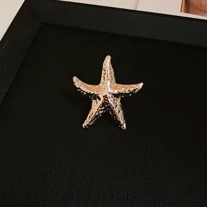 Detailed view of a golden wrinkled metal starfish stud earring on black backdrop