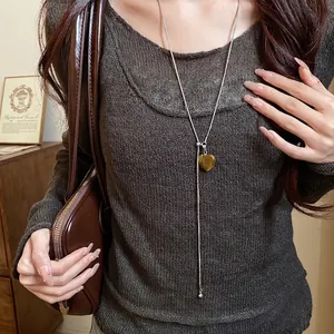 Elegant long silver necklace with heart-shaped tiger eye pendant worn by a stylish model.