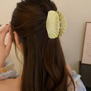A close-up view of a pearlescent shell-shaped hair claw clip on long wavy brown hair