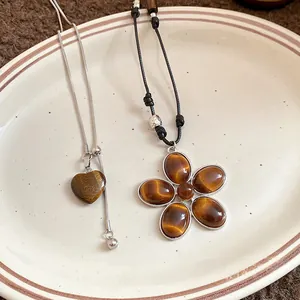 Macro view of vintage tiger eye heart and five-petal flower necklaces on a ceramic plate