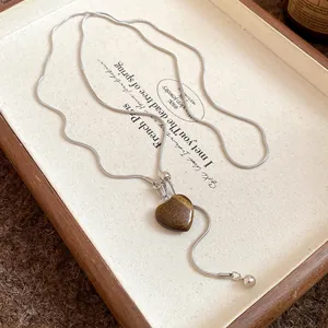 Close-up detail of vintage silver snake chain necklace with brown heart stone pendant