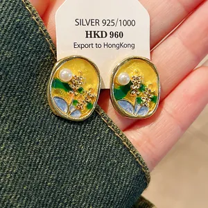 Detail shot of enamel floral earrings with a delicate pearl on silver needles.