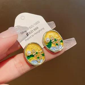 Close-up of artistic enamel landscape earrings with pearl and golden flower accents.