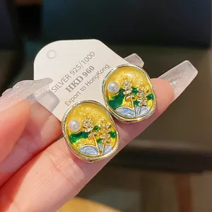 Close-up of elegant floral enamel earrings with pearls and silver posts.