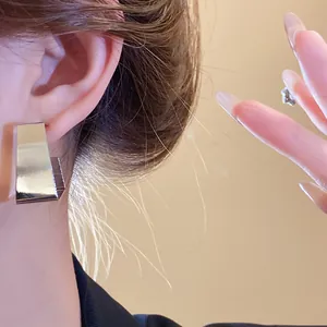Close-up detail of minimalist silver geometric trapezoid ear studs worn on a model's ear.